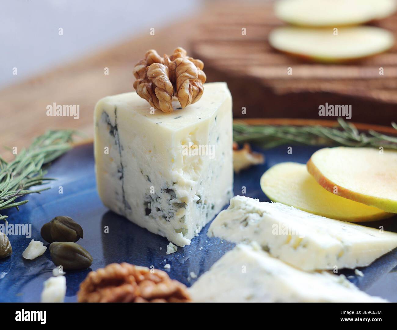 Formaggio blu con noci, capperi e rosmarino in un piatto su un tavolo Foto Stock