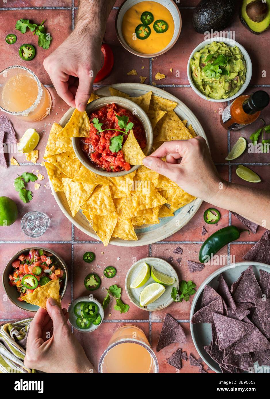 Vista dall'alto mani con patatine, salsa, guacamole, bevande su piastrelle. Foto Stock