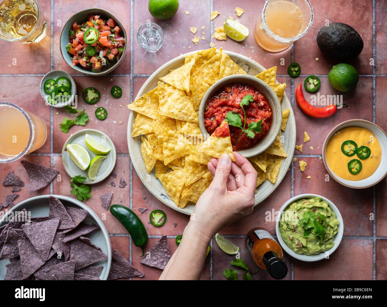 Vista dall'alto, tuffando a mano il chip nella salsa con guacamole, bevande su piastrelle. Foto Stock
