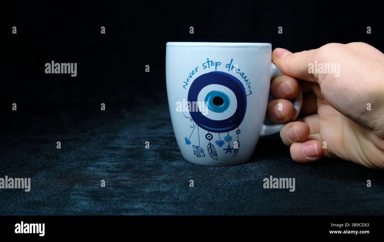 Tazza di caffè del mattino con amuleto oculare in mano Foto Stock