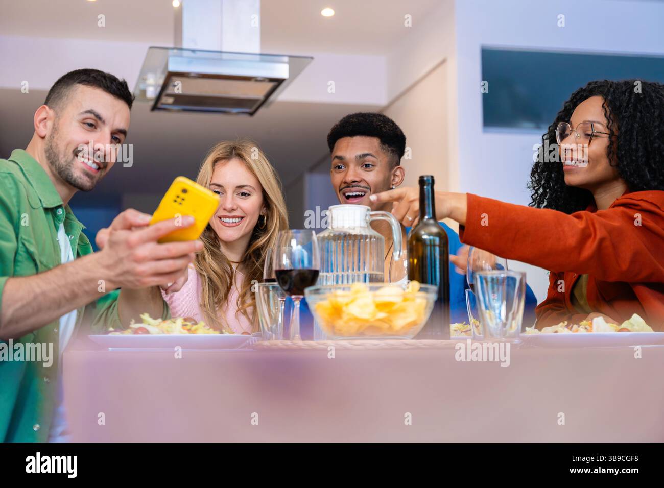 Amici multietnici felici gustando spuntini e bevande in una cucina moderna e luminosa Foto Stock
