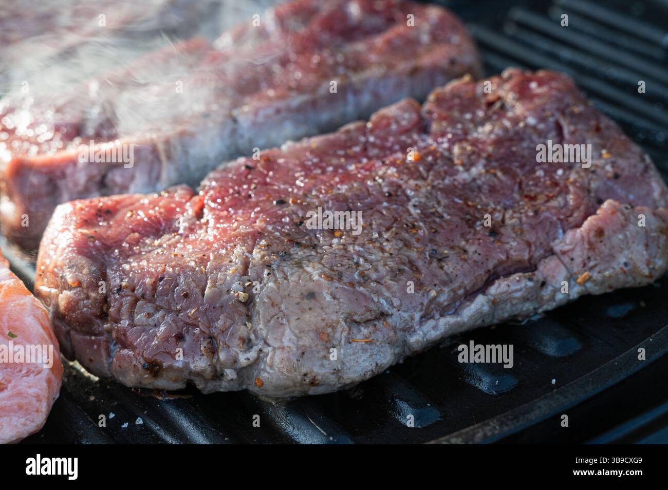 Le succose bistecche sfrigolano deliziosamente su una griglia calda, mostrando i loro sapori succulenti e ricchi Foto Stock