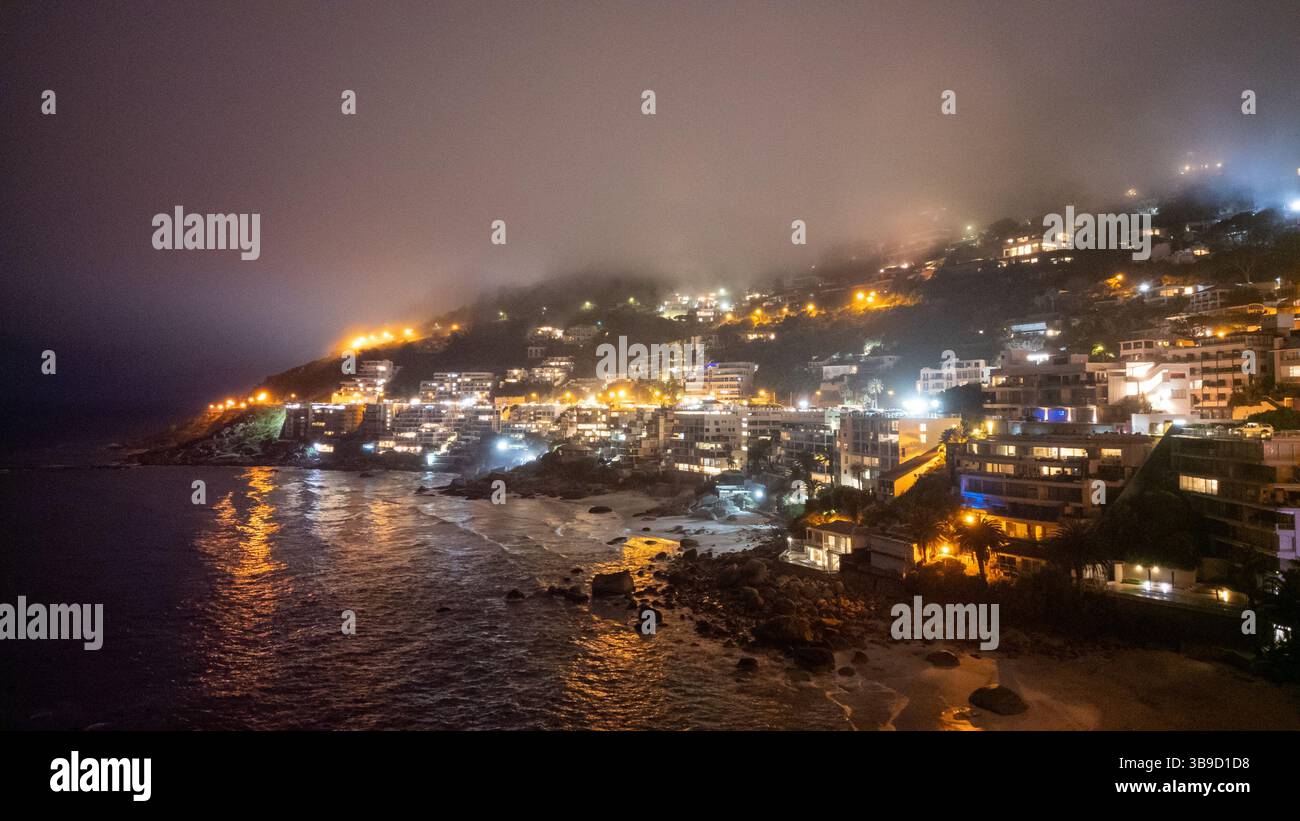 Una splendida vista della costa di Camps Bay di notte, illuminata dal bagliore delle luci della città che si riflettono sull'oceano. Foto Stock