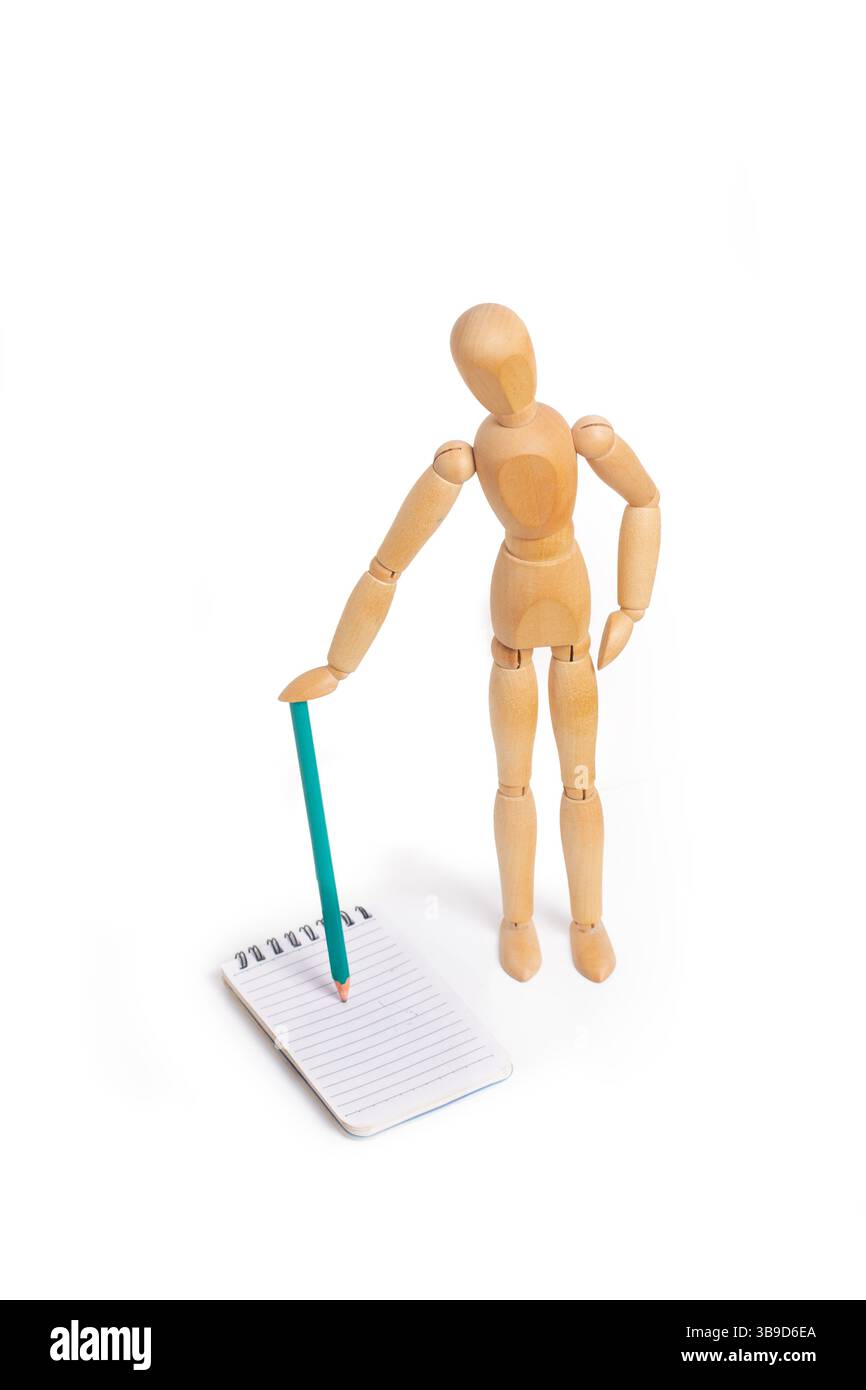 Un giocattolo manichino di legno che regge una matita su un quaderno a spirale su sfondo bianco con spazio per le copie Foto Stock
