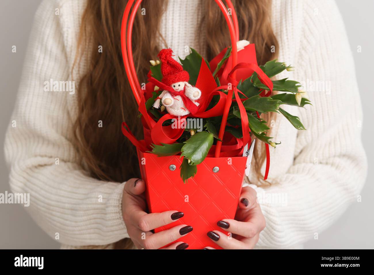 Cestino floreale per le vacanze invernali. Decorazioni natalizie rosse. Disposizione dei fiori di Natale. Piccolo giocattolo pupazzo di neve. Donna che tiene il centrotavola stagionale. Foto Stock