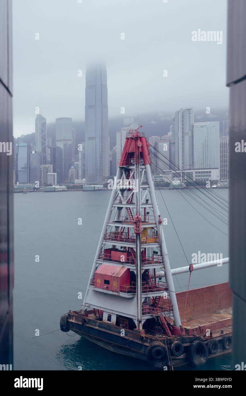 Chiatta di costruzione attraccata nel Victoria Harbour con lo skyline coperto di nebbia sullo sfondo Foto Stock