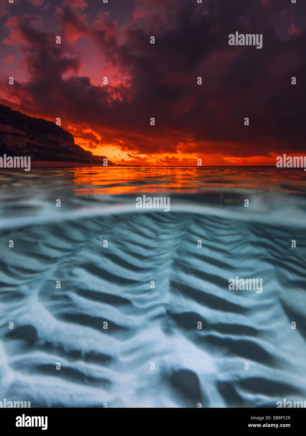 Tramonto sull'oceano calmo con motivi di sabbia subacquea, catturato in un paesaggio marino diviso Foto Stock