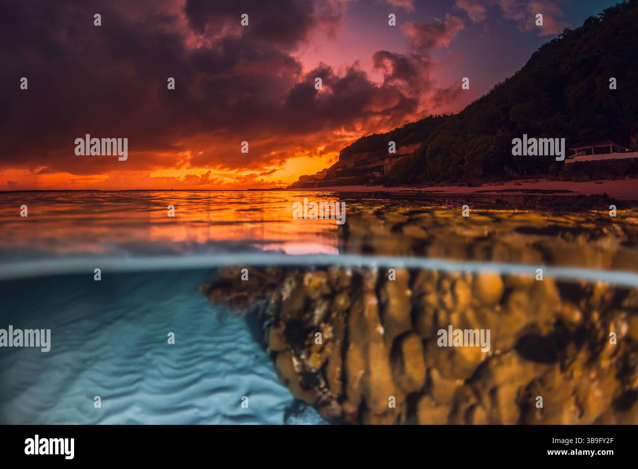 Spettacolare tramonto o alba sul mare calmo con motivi di sabbia e coralli sott'acqua, catturati in un paesaggio marino diviso Foto Stock