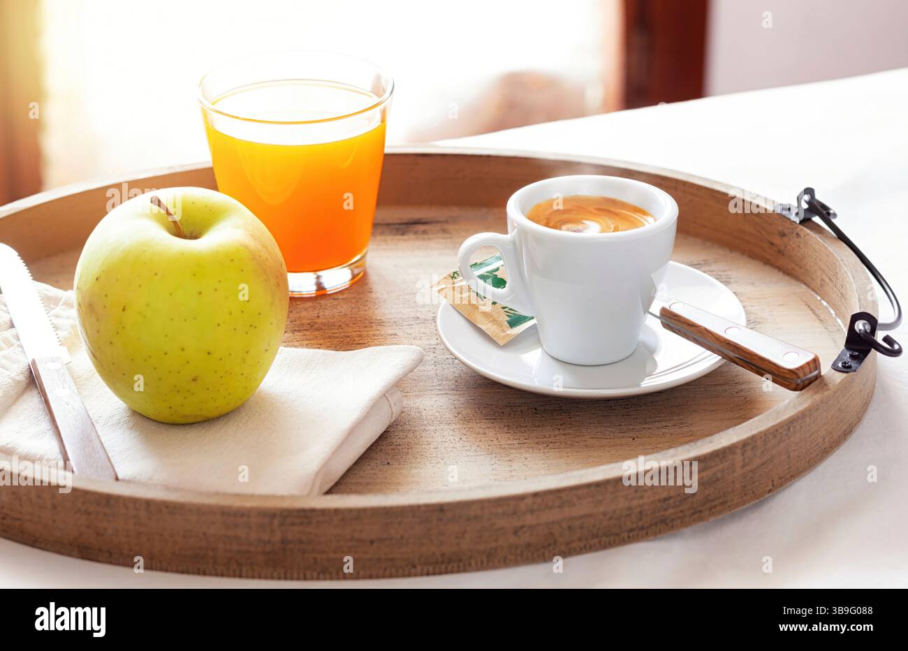 Vassoio in legno con colazione fresca con caffè, succo di frutta e una mela croccante, servito in un'accogliente camera d'hotel, crogiolandosi alla luce calda del sole per una perfetta esperienza mattutina Foto Stock
