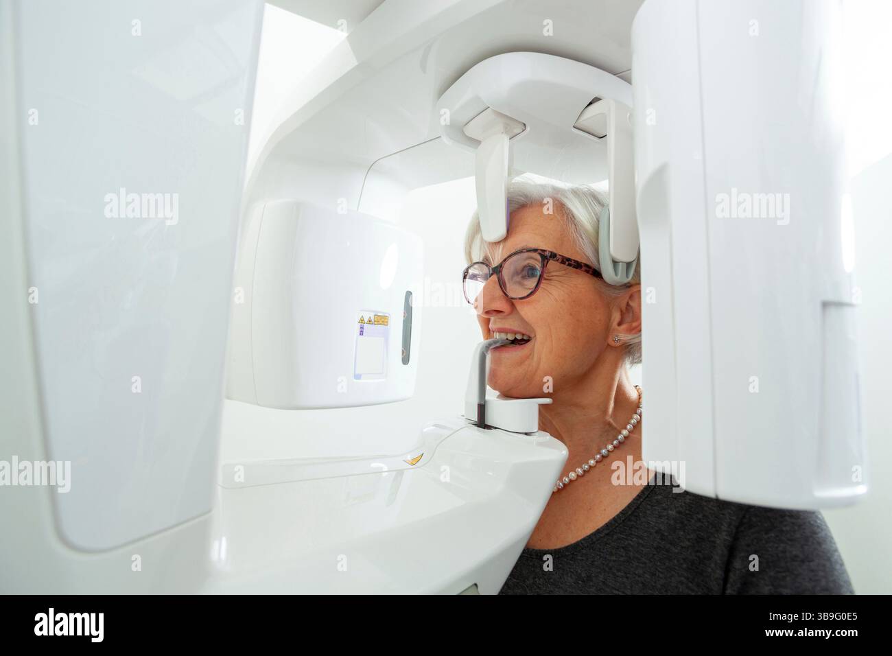 Donna anziana che riceve un esame radiografico dentale panoramico in una clinica odontoiatrica all'avanguardia, evidenziando la tecnologia moderna nell'assistenza sanitaria orale Foto Stock
