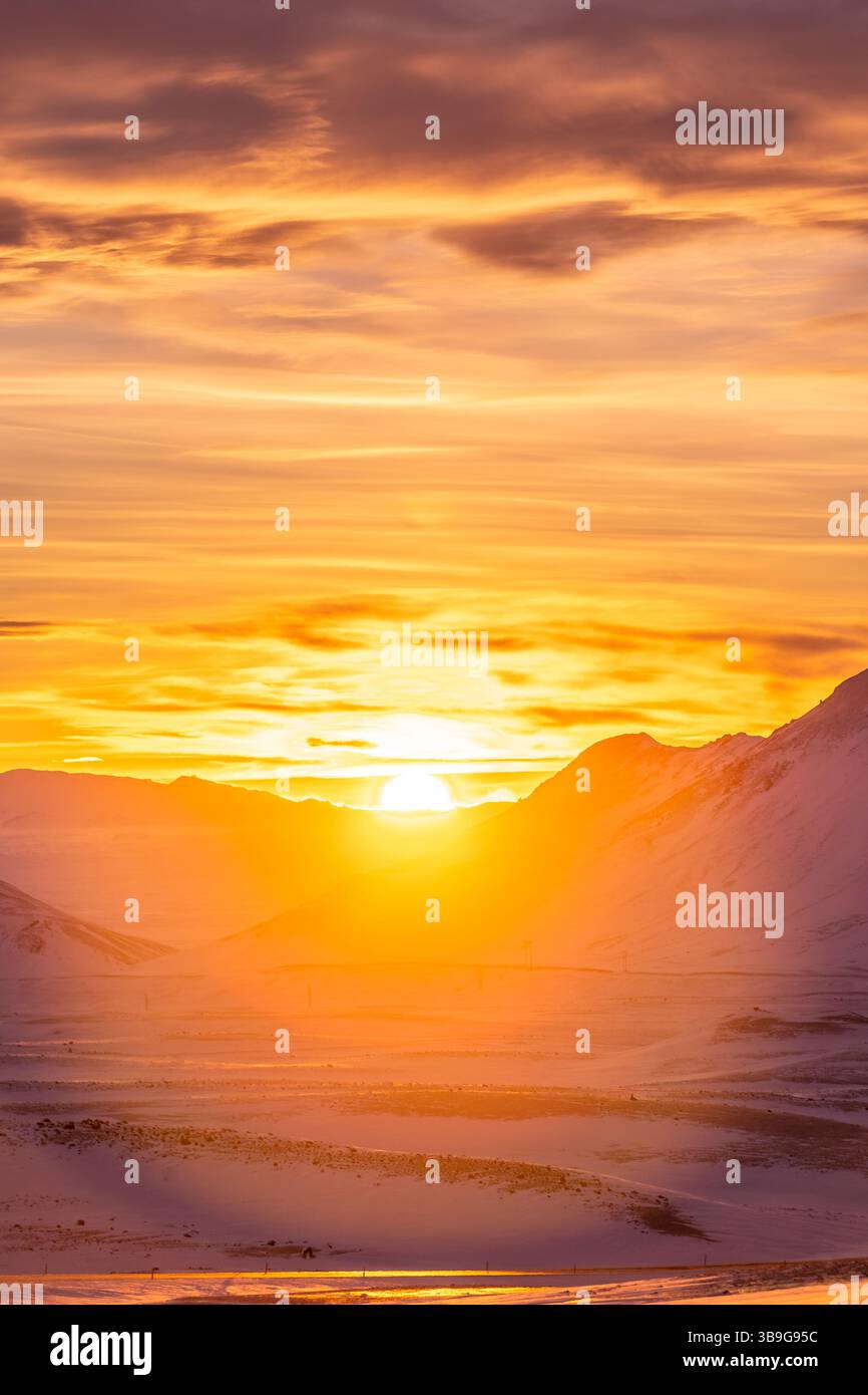 Una vista mozzafiato di un vibrante tramonto invernale che illumina le montagne innevate in Islanda. I colori caldi contrastano il paesaggio ghiacciato, creando un Foto Stock