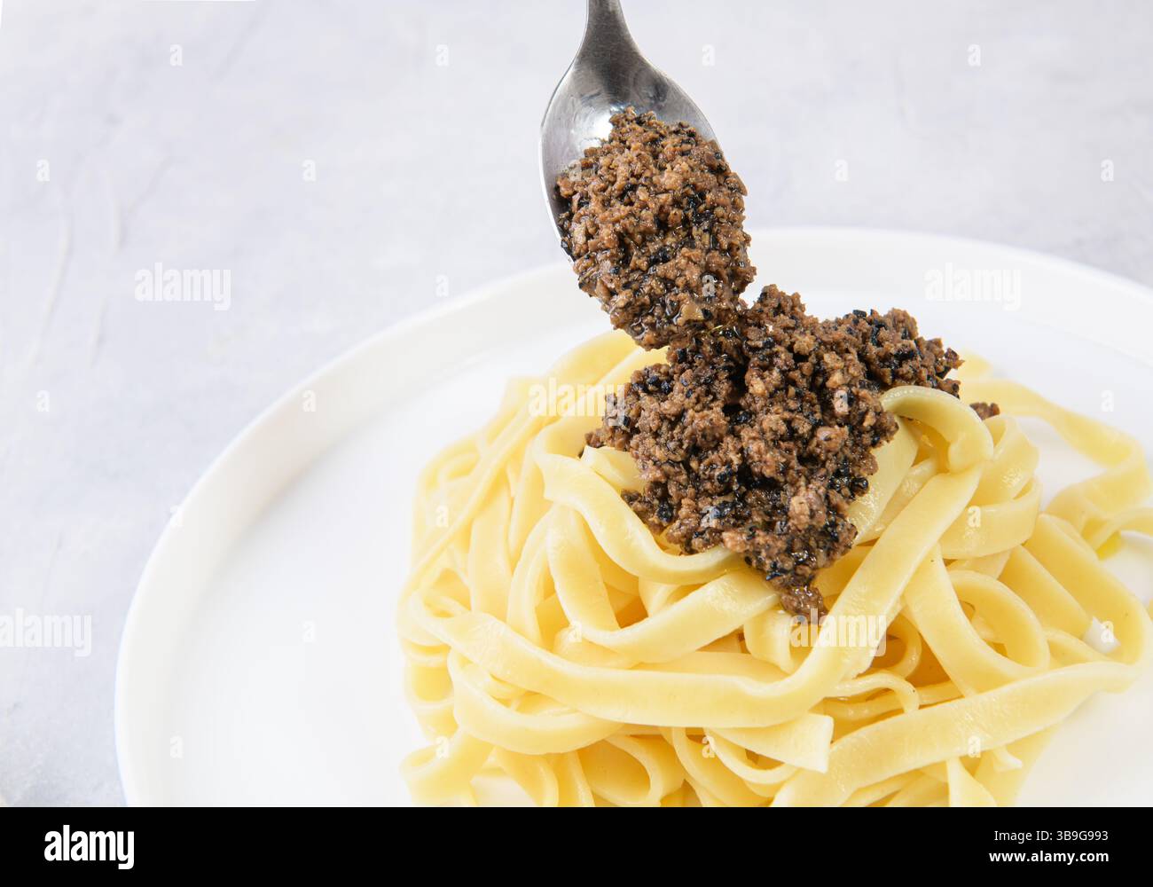 Un cucchiaio di salsa di tartufo nero salato aggiunto a una ciotola di pasta fresca. Perfetto per un'esperienza culinaria gourmet, catturando l'essenza di Italia Foto Stock