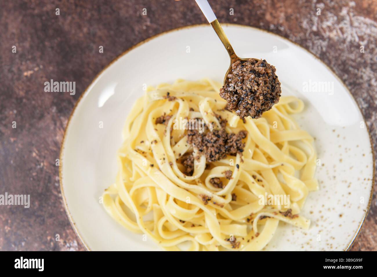 Tagliatelle con tartufo nero tritato sul cucchiaio, focalizzazione selettiva. Ricetta autunnale italiana fresca con tartufo nero su tavola marrone in elegante Foto Stock
