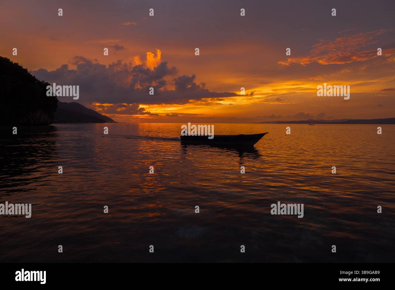 Un tramonto sereno dipinge il cielo con sfumature di arancione e viola sull'isola di Kri, l'arcipelago di Raja Ampat. Una piccola barca e il suo occupante solitario galleggiano tranquillamente Foto Stock