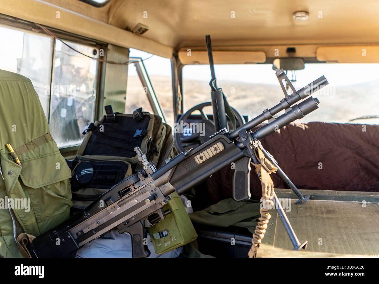 All'interno di un veicolo militare, dotato di equipaggiamento tattico e arma da fuoco. Dotato di attrezzature da combattimento robuste e pronte all'uso in luce naturale. Foto Stock