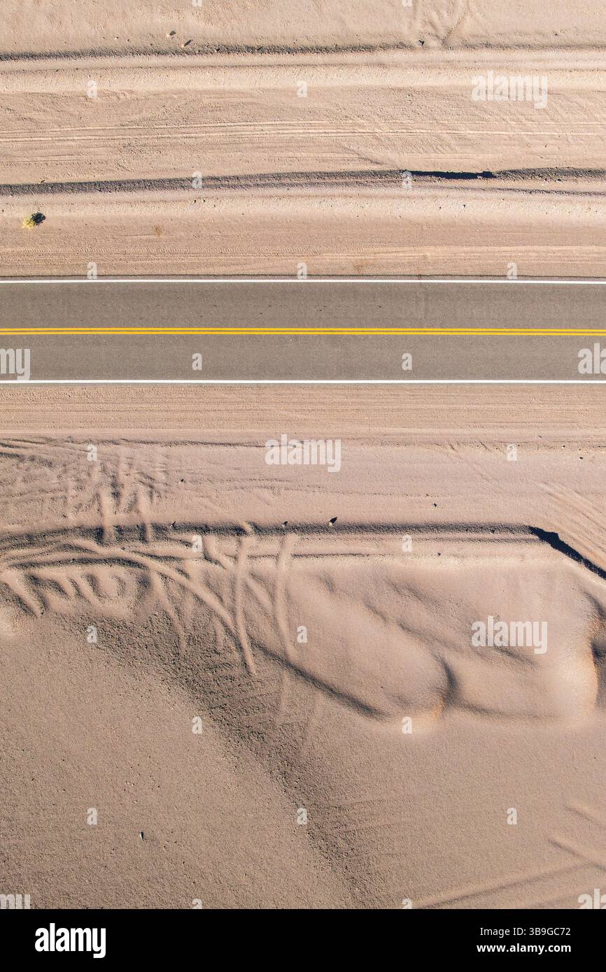 Vista aerea di una strada asfaltata dritta che attraversa un paesaggio desertico sabbioso della Puna argentina. La strada è accompagnata da intricati schemi i Foto Stock