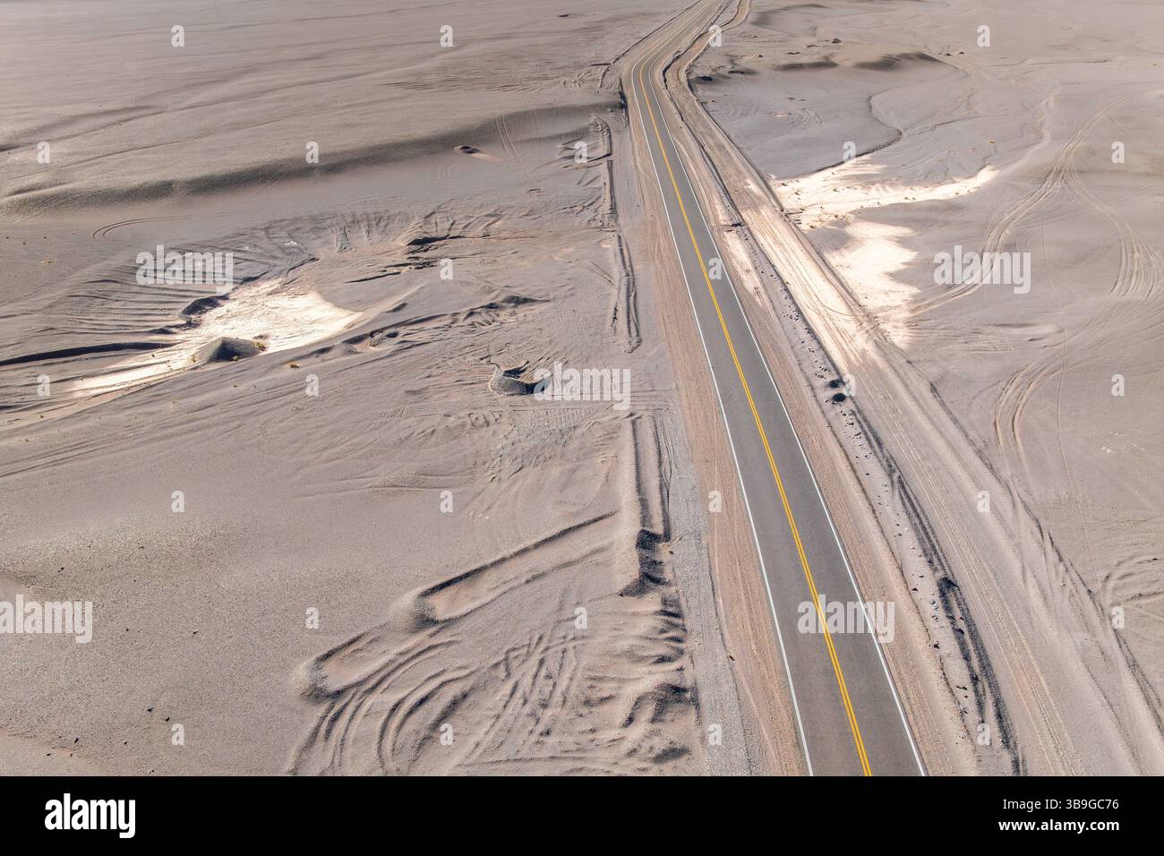 Vista aerea di una lunga e solitaria strada asfaltata che attraversa un vasto paesaggio desertico della Puna argentina. La scena cattura la vastità e. Foto Stock