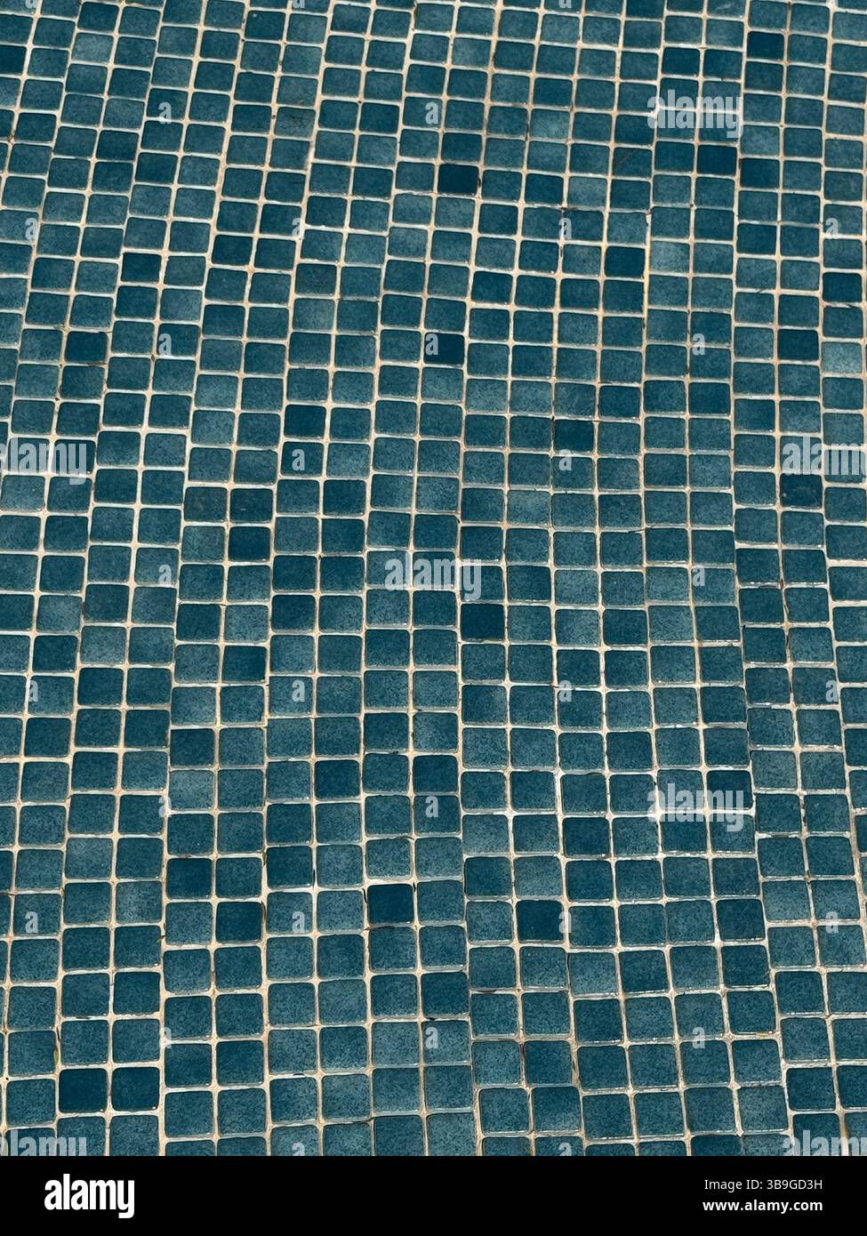 Questa immagine mostra un motivo a mosaico blu irregolare composto da piccole piastrelle quadrate. Il design testurizzato crea un effetto ondulato, aggiungendo profondità e visibilità Foto Stock