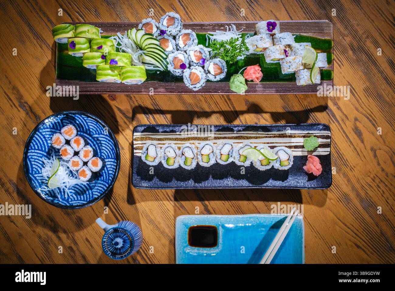 Vista dall'alto di una varietà di coloratissimi sushi roll serviti su piatti decorativi, pronti da gustare con salsa di soia e bacchette, creando un vivace culin Foto Stock