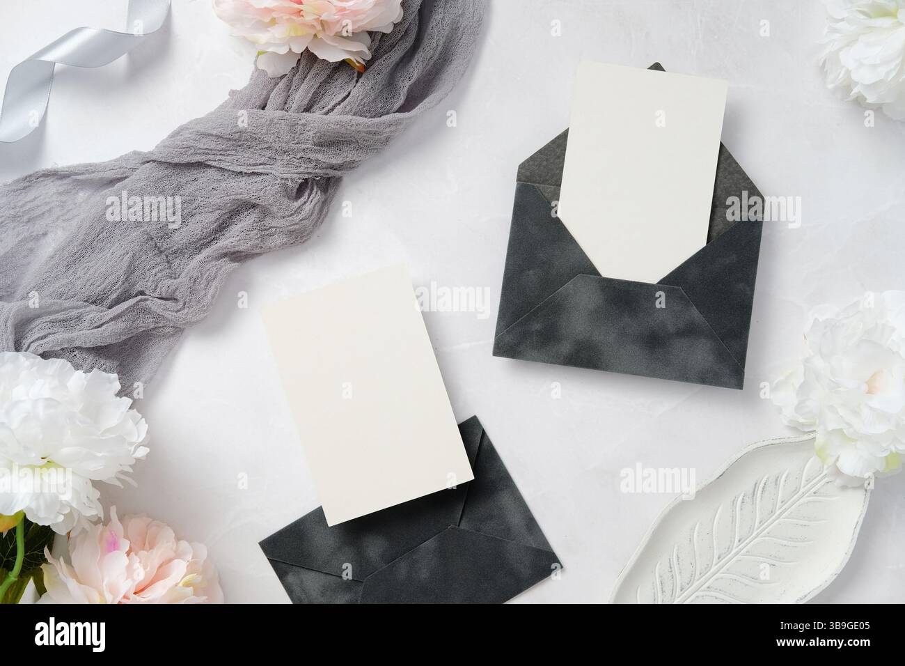 Un sofisticato layout di cartoleria per matrimoni con eleganti buste scure, biglietti d'auguri, delicati fiori e tessuti morbidi, perfetto per inviti o ricevimenti Foto Stock