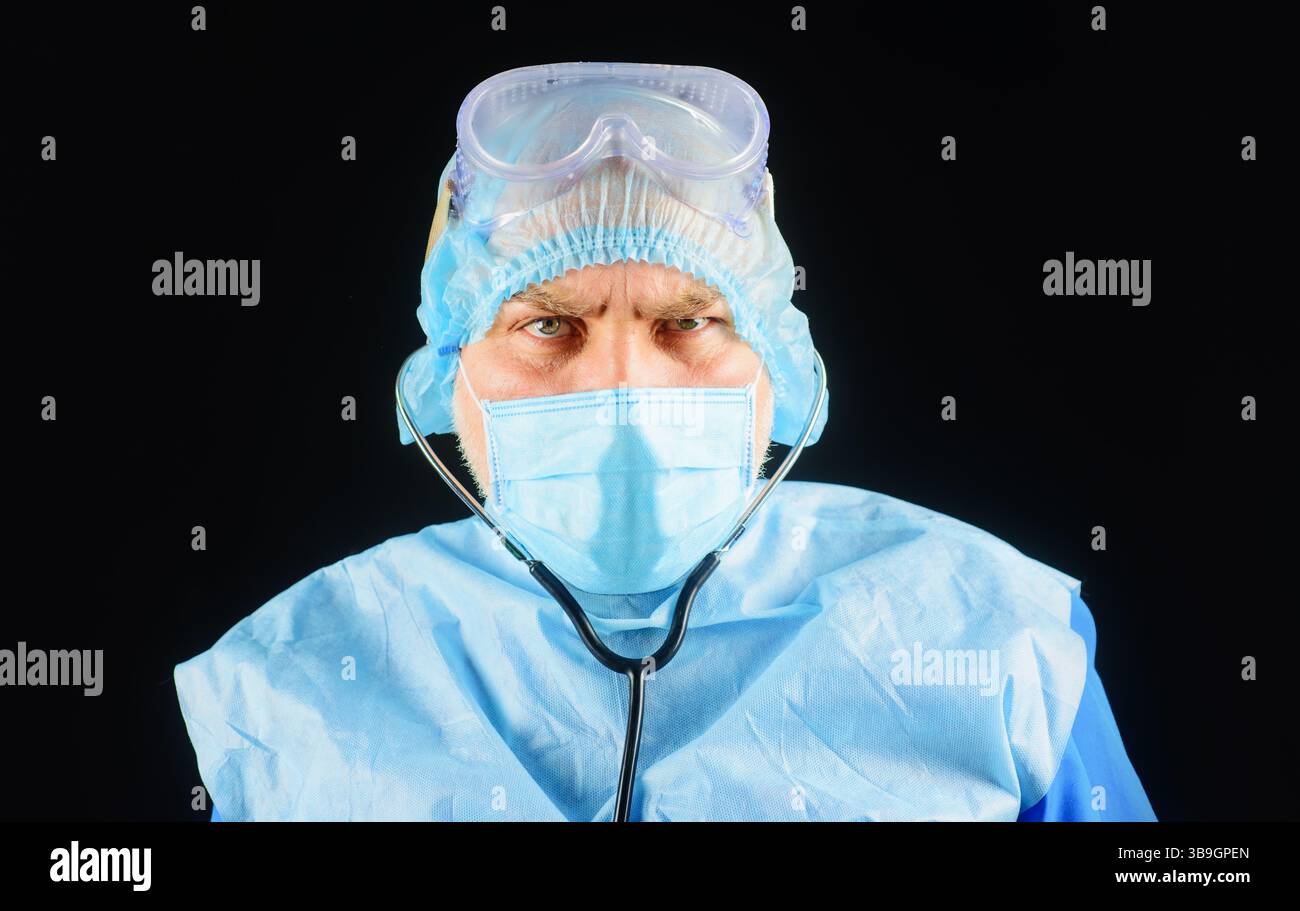 Primo piano ritratto di medico serio in tuta protettiva, maschera medica e occhiali di sicurezza con stetoscopio. Medico, medico in uniforme medica con ste Foto Stock