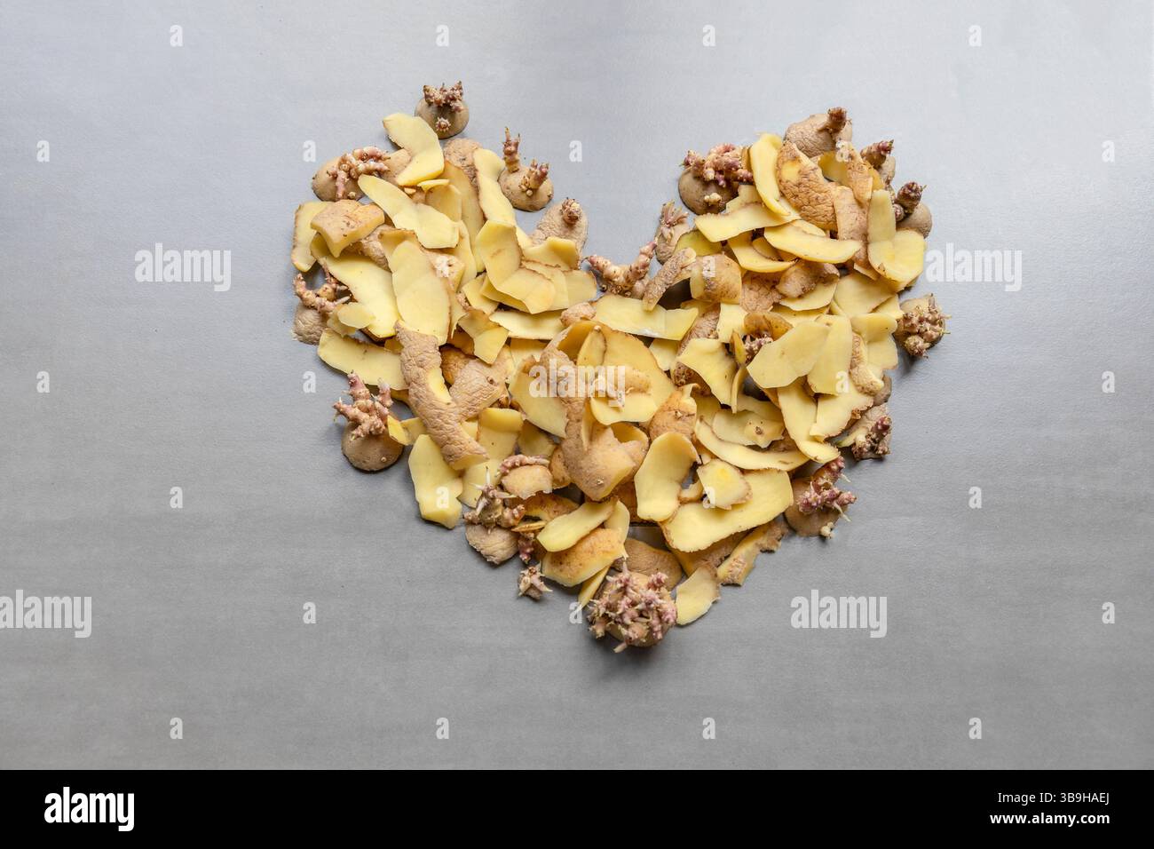 I frammenti di patate e le pelature si trovano a forma di cuore su sfondo grigio sul tema dei rifiuti organici e della separazione organica Foto Stock