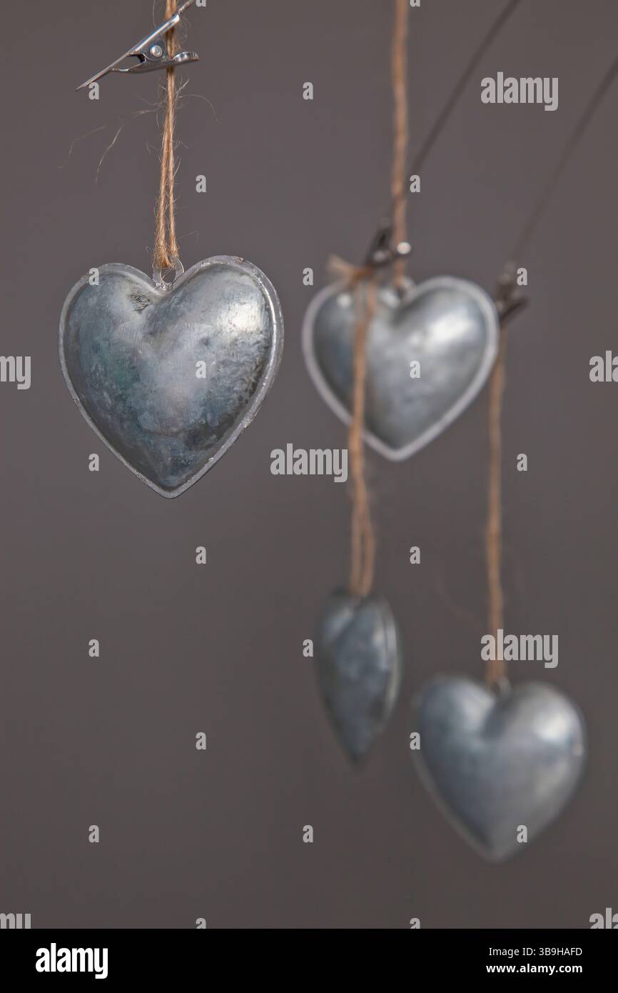 Cuori in metallo color argento appesi su corde in primo piano su sfondo grigio come messaggio simbolico e decorazione per il matrimonio Foto Stock