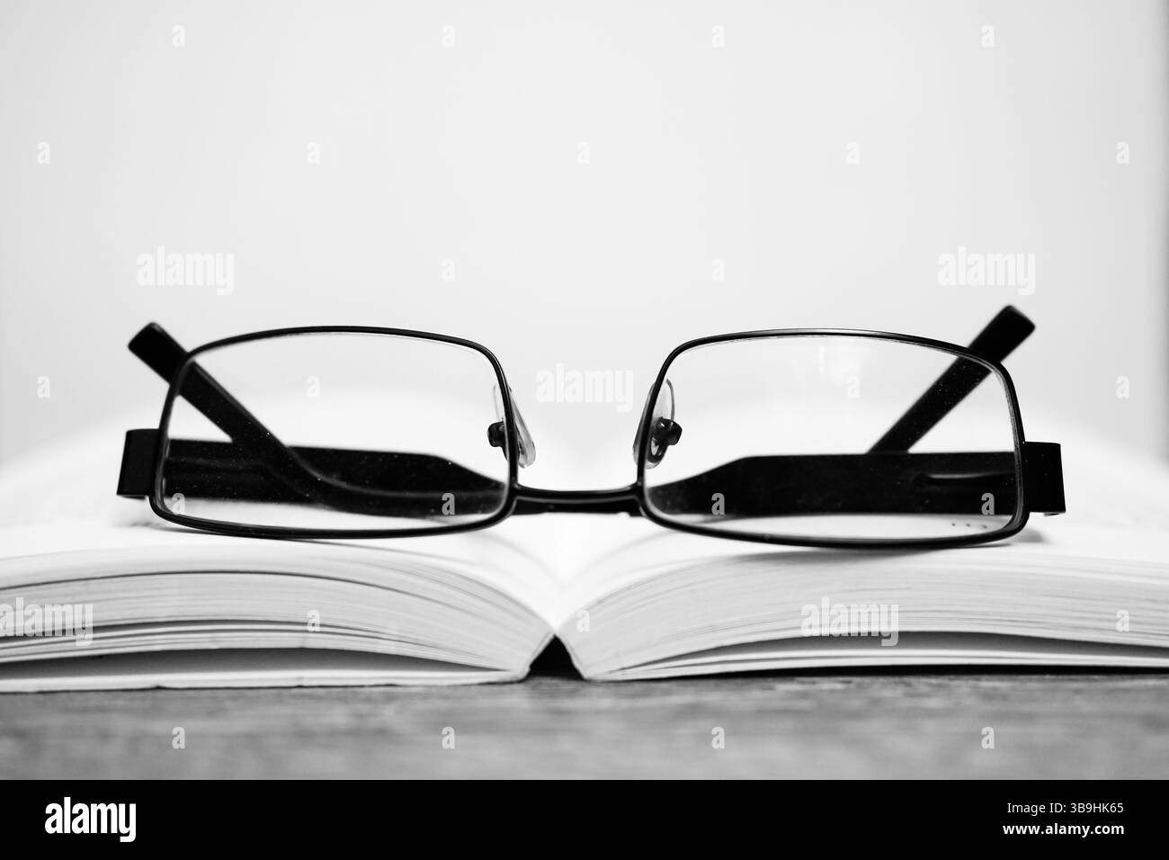 Un paio di occhiali è sopra un libro. Gli occhiali sono neri e il libro è bianco Foto Stock