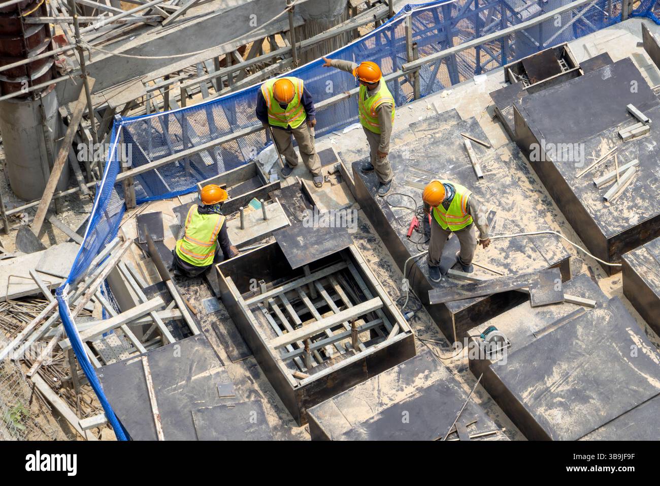 Gruppo di operai edili che indossano giubbotti di sicurezza e caschi che lavorano su un quadro di costruzione. Foto Stock