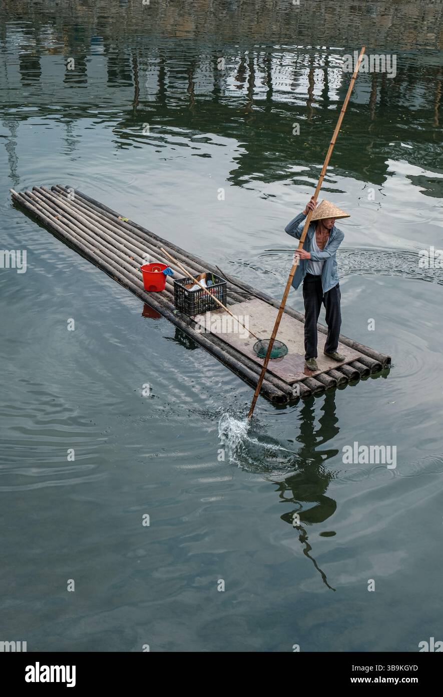 Barcaiolo che indossa un cappello di paglia pagaiando una zattera di bambù sull'acqua verde del fiume a Jingdezhen, Jiangxi, Cina Foto Stock