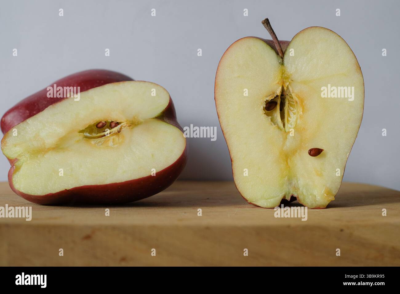 Meles Red Prince posto su un tagliere di legno. La mela tagliata a metà ha una polpa di colore giallo chiaro con semi, a indicare la freschezza e lo stato conservato. Foto Stock