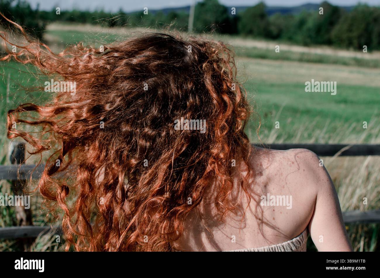 Primo piano di capelli rossi ricci selvatici che soffiano nel vento mentre la donna si muove liberamente in campo estivo, catturando energia naturale pura libertà di movimento e rurale Foto Stock