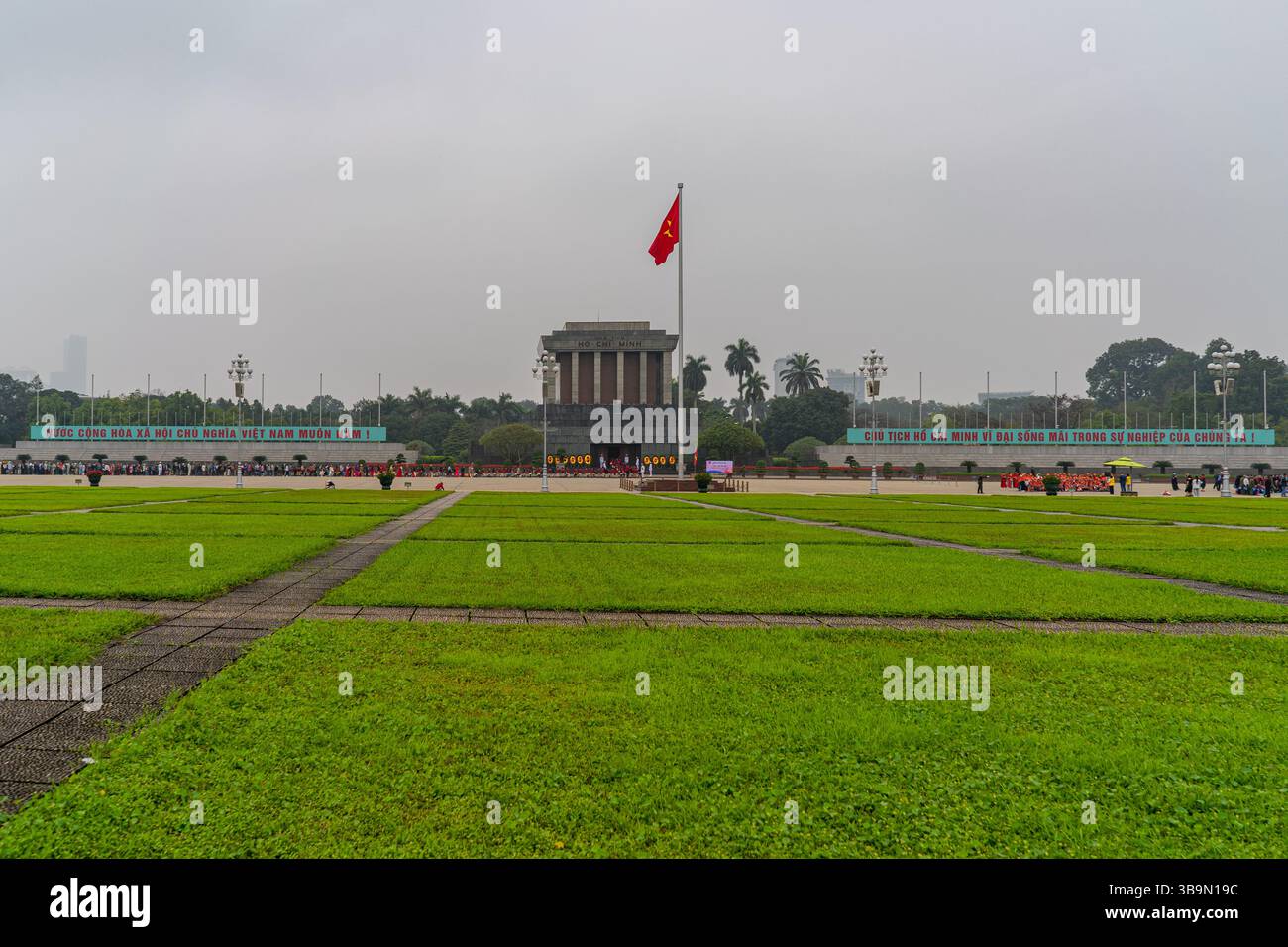 Vista del Mausoleo di ho chi Minh ad Hanoi, con la bandiera vietnamita che sventolava. Il vasto prato in primo piano conduce al punto di riferimento storico. Foto Stock
