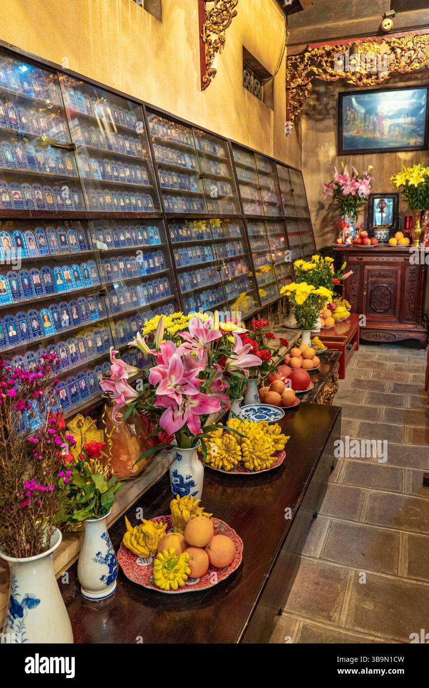 Un'immagine interna mostra una mostra di monumenti commemorativi, fiori vivaci e offerte, che riflettono le tradizioni vietnamite. La scena è piena di cultura Foto Stock