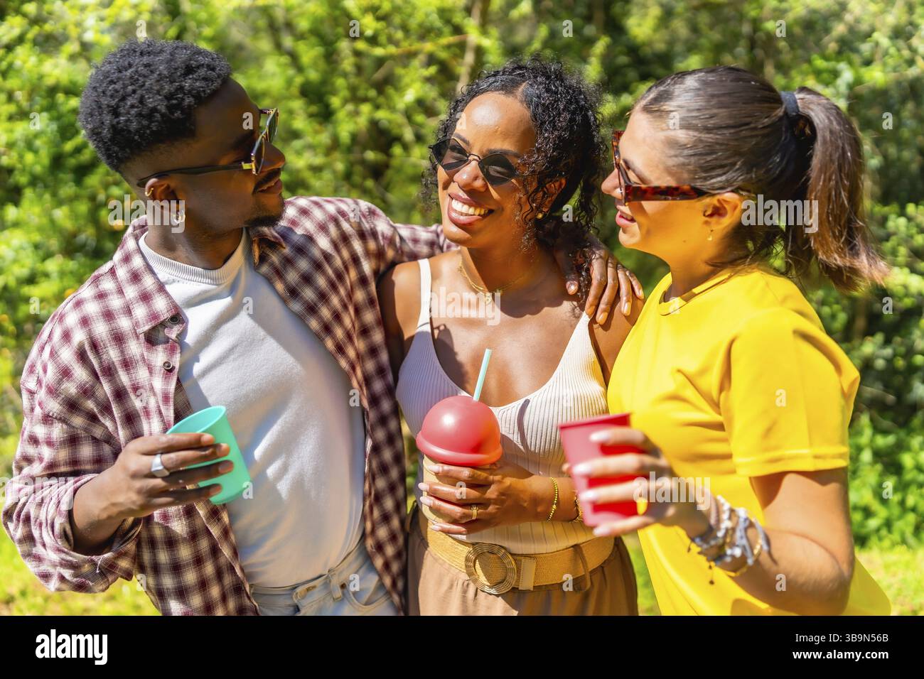 Tre giovani amici multietnici si godono una giornata di sole all'aperto, sorseggiando un drink Foto Stock