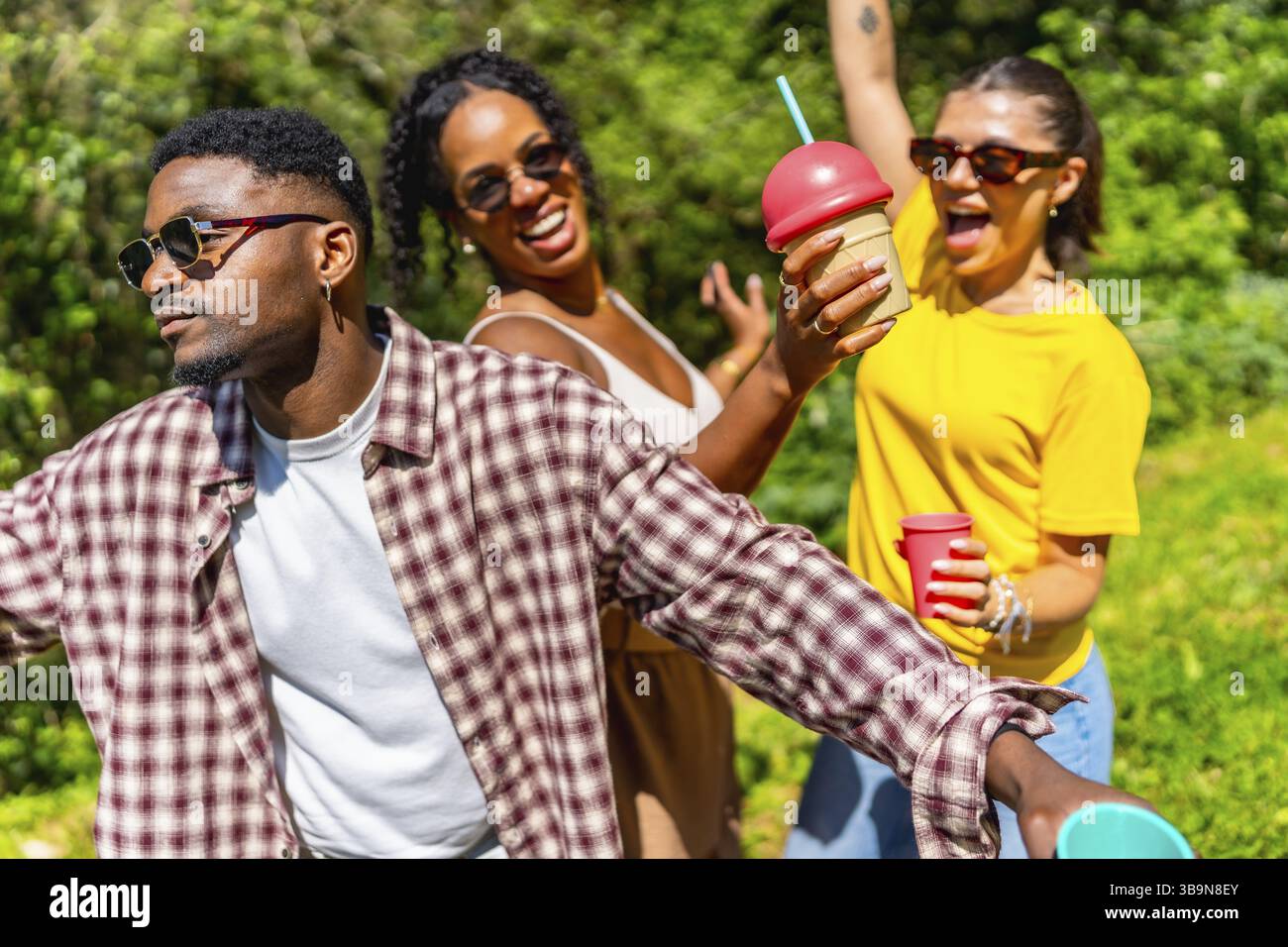 Tre amici si godono il sole estivo, ballano con gioia sorseggiando bevande fredde e condividendo le risate in un vivace ambiente all'aperto Foto Stock