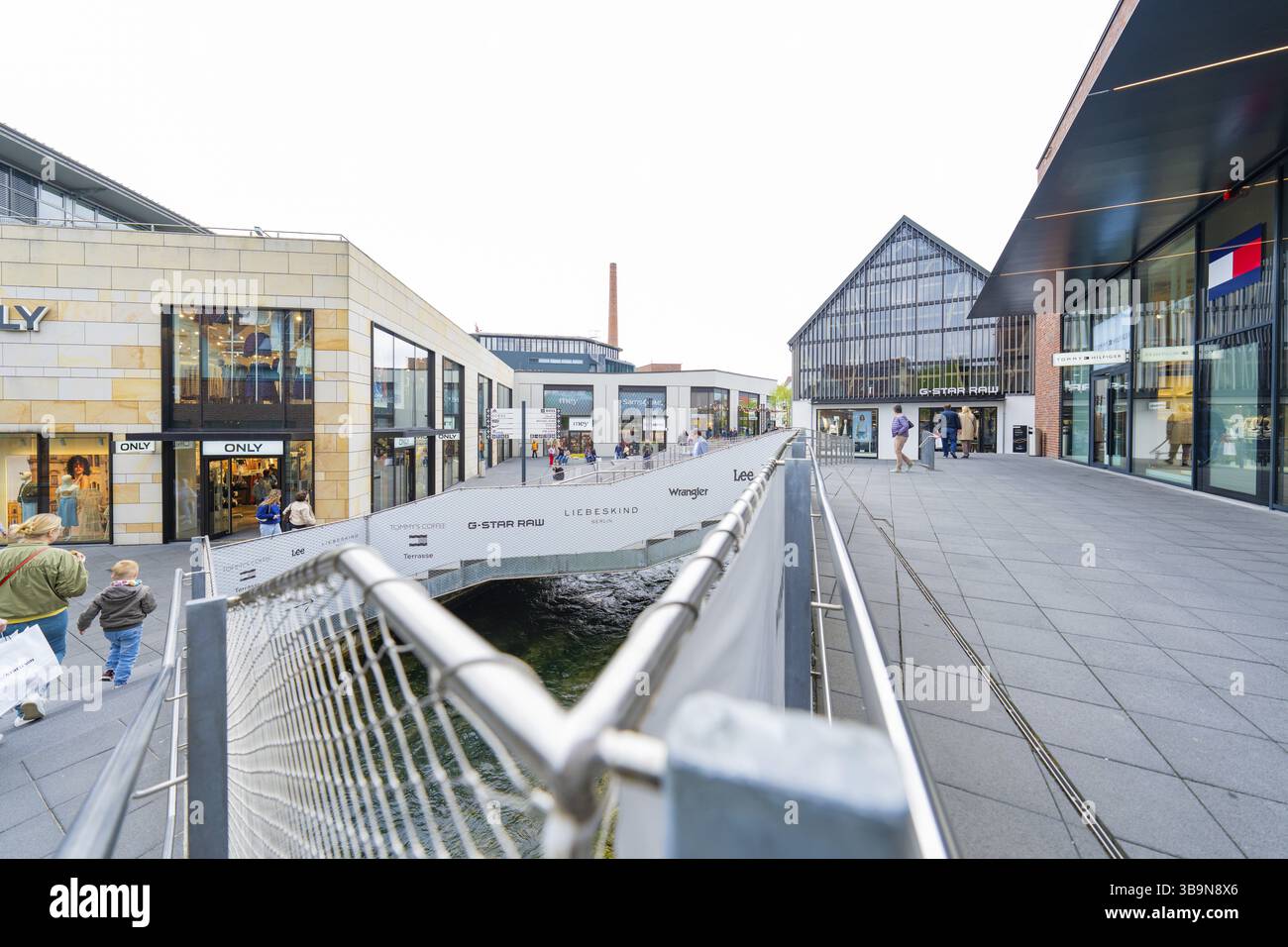 Area urbana moderna con negozi con facciata in vetro e un piccolo ponte, Outlet City Metzingen, Germania, Europa Foto Stock