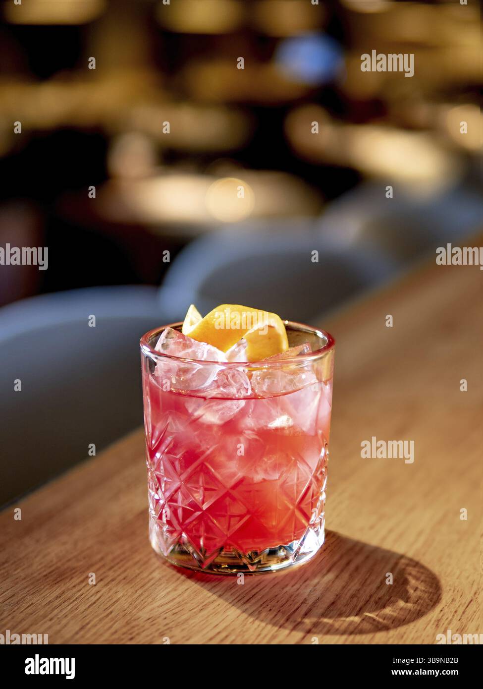Cocktail alcolico rosa trasparente con ghiaccio, aperol e gin sul bancone del bar all'interno del ristorante. Cocktail alcolici decorato a spirale con scorza d'arancia. Freddo Foto Stock