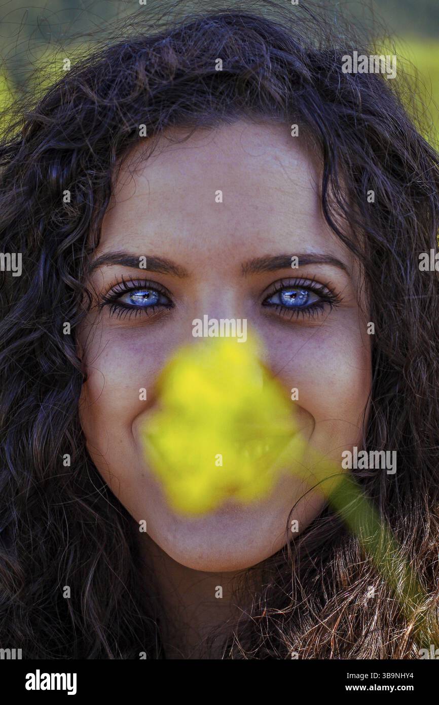 Ritratto ravvicinato di una giovane donna dagli occhi blu dietro un fiore giallo Foto Stock
