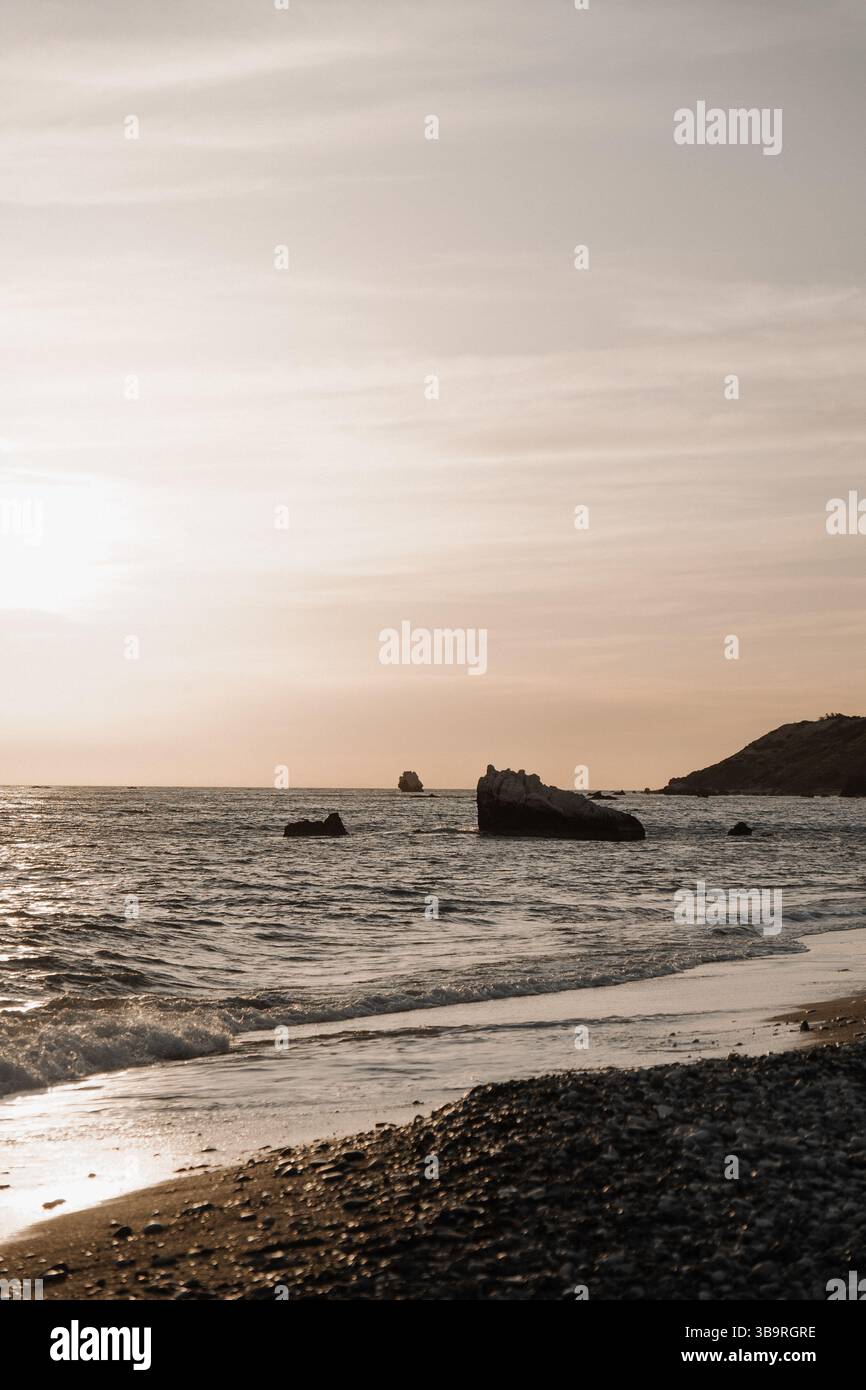 Tramonto sul mare con rocce in acqua e dolci onde che bagnano la riva, atmosfera tranquilla e tranquilla. Foto Stock
