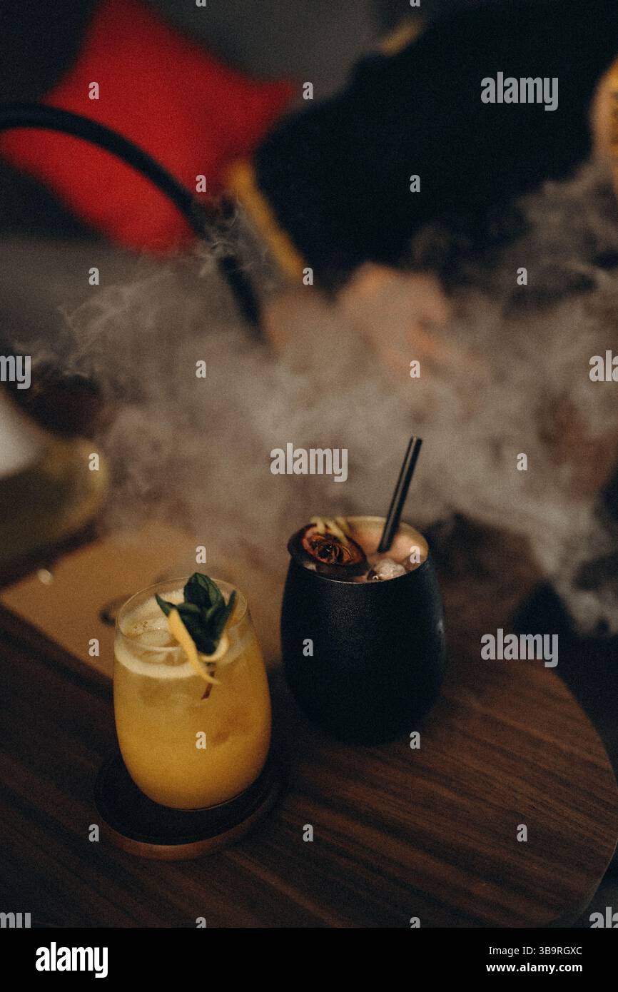 Eleganti cocktail affumicati serviti su un tavolo di legno in un bar scuro con illuminazione soffusa e ricchi dettagli. Foto Stock