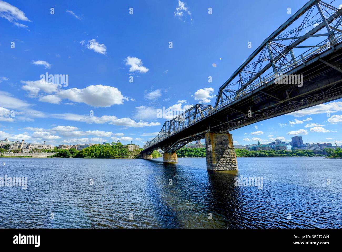 Il ponte a capriata in acciaio attraversa un ampio fiume sotto un cielo azzurro limpido con nuvole sparse, creando un'audace vista architettonica e panoramica. Foto Stock
