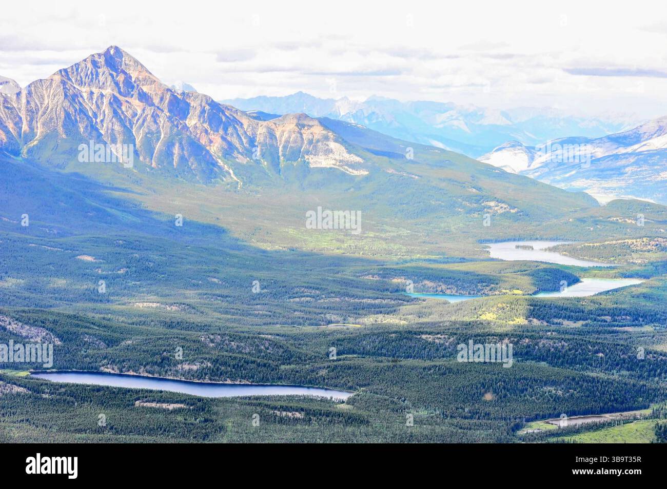 Maestoso paesaggio montano con creste a strati, fitta foresta verde e laghi tortuosi sotto un cielo luminoso, perfetto per la natura e gli sfondi di viaggio. Foto Stock