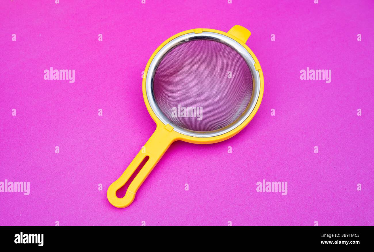 Un filtro per tè giallo o da cucina con maglie sottili posizionato su uno sfondo rosa brillante, isolato e girato dall'alto. Foto Stock