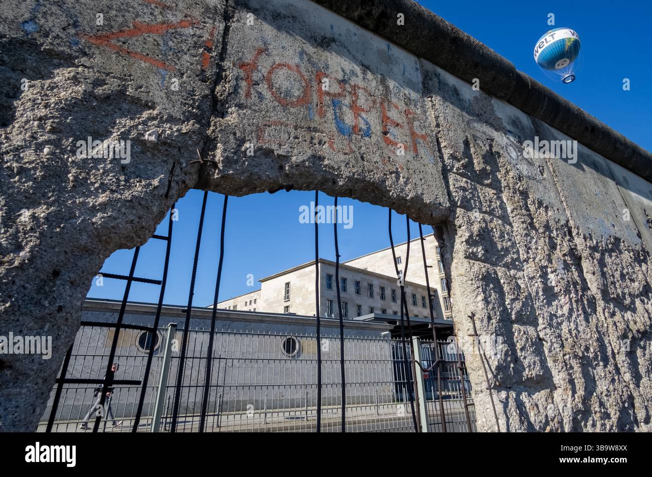 Segmento incrinato del muro di Berlino con armatura esposta e mongolfiera Welt nel cielo, catturato nel centro di Berlino. Foto Stock
