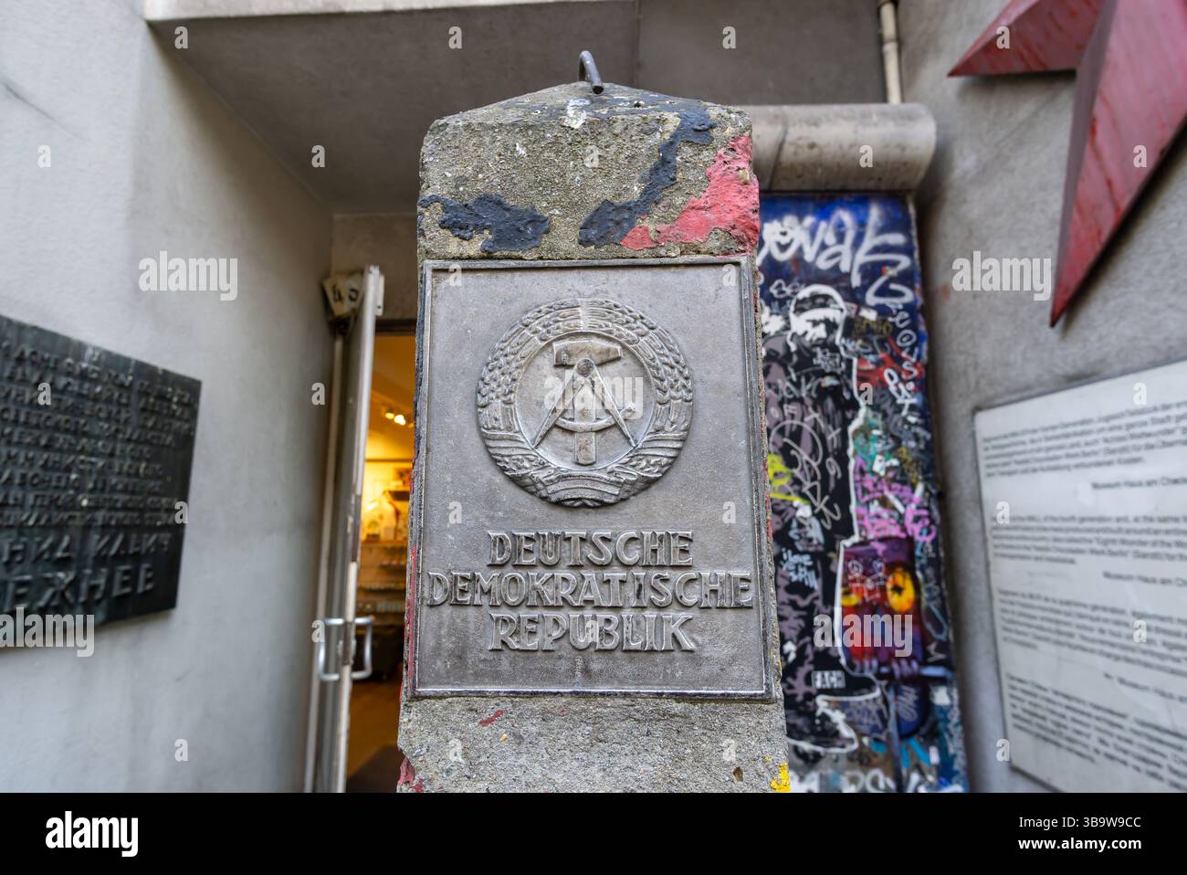 Palo in cemento con lo stemma della Repubblica Democratica tedesca presso il Museo del muro di Berlino vicino al Checkpoint Charlie. Foto Stock