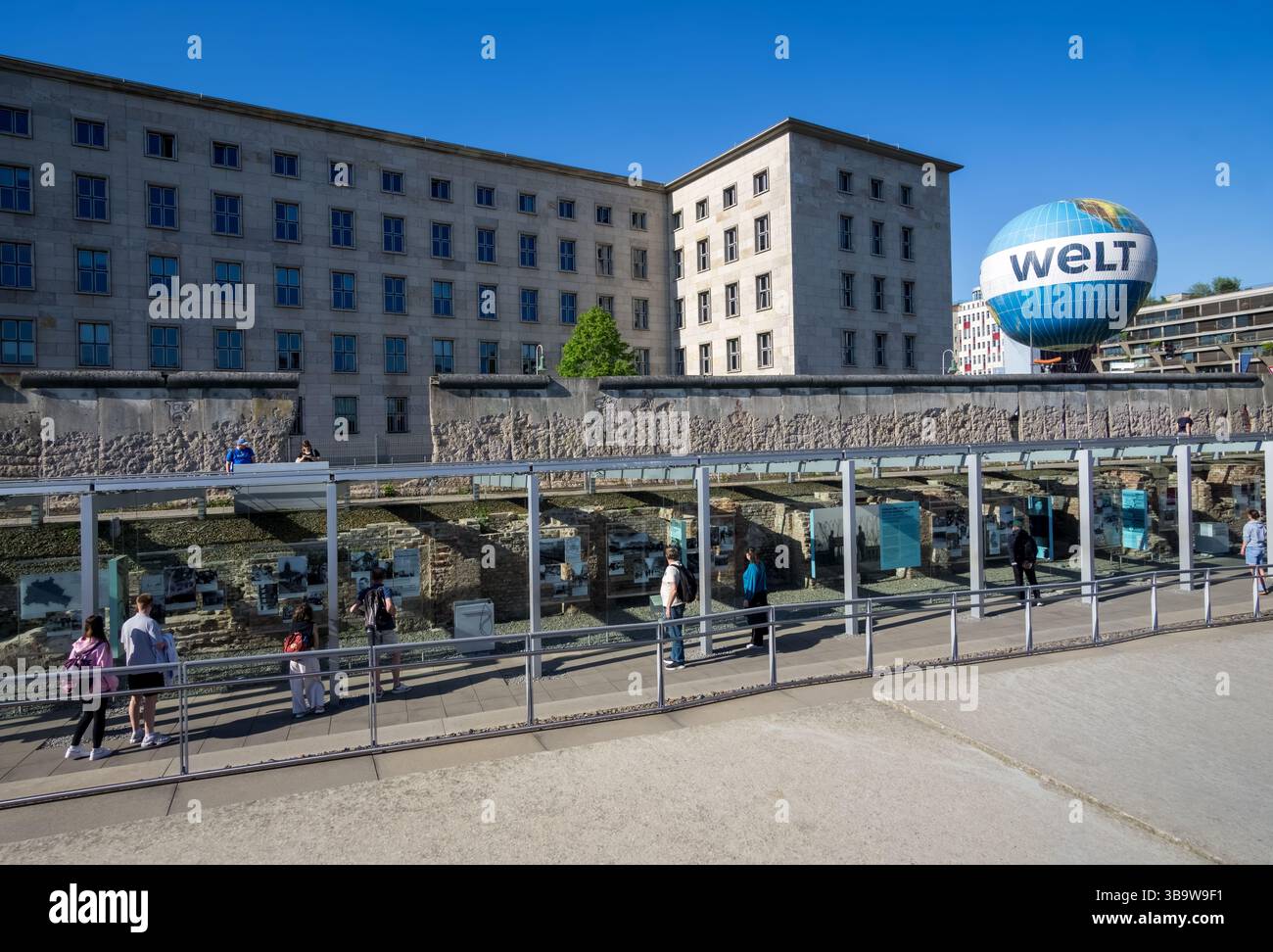 Persone alla mostra all'aperto del sito commemorativo della topografia del terrore con il muro di Berlino e il paesaggio urbano sullo sfondo. Foto Stock