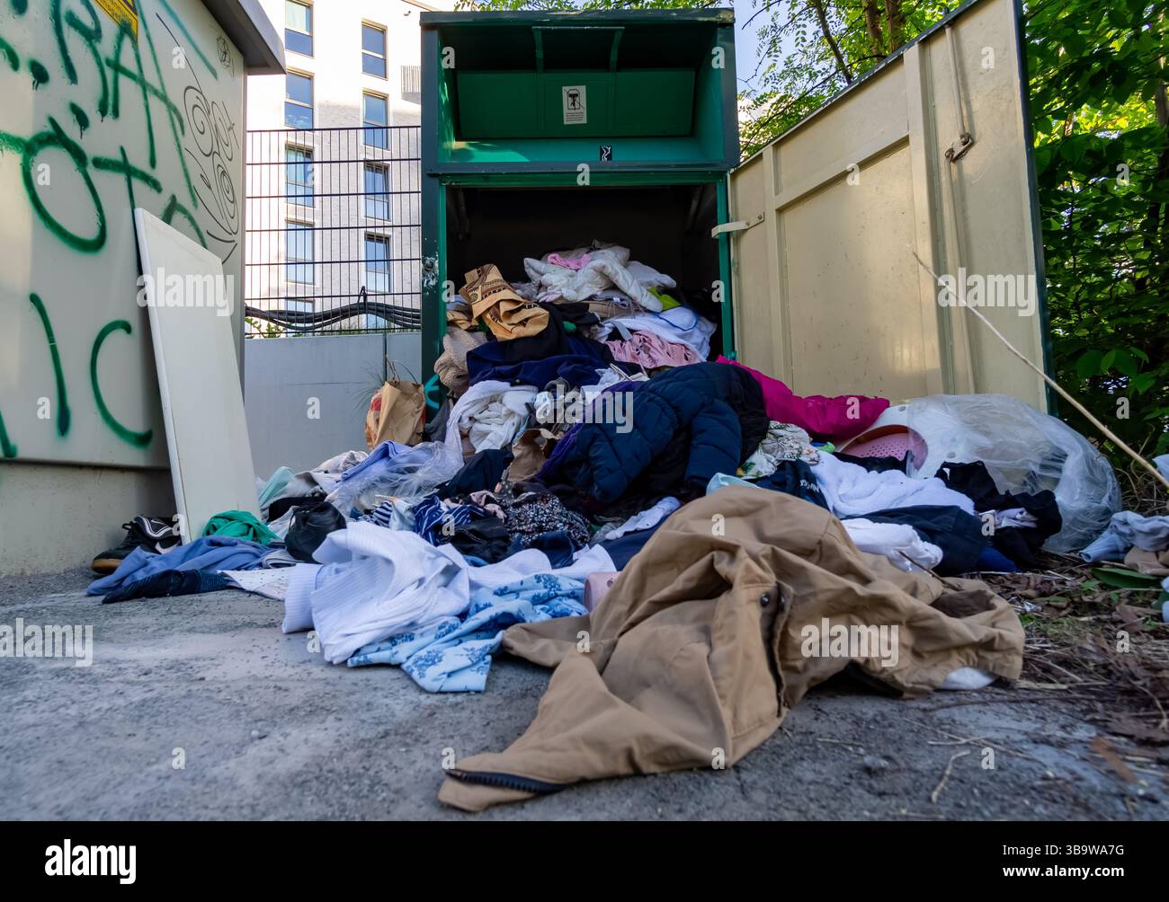 Traboccante o forse saccheggiato cestino di donazione di abbigliamento con indumenti sparsi all'esterno di un container a Berlino, Germania. Foto Stock