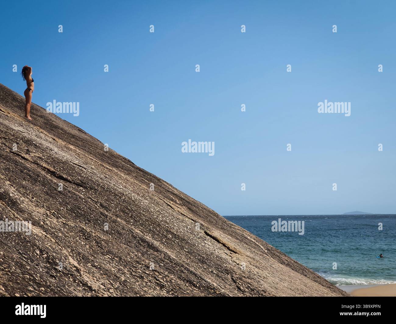 Donna in piedi sulla Rocky Slope con vista sull'oceano a Itacoatiara Beach - Niterói, Brasile Foto Stock