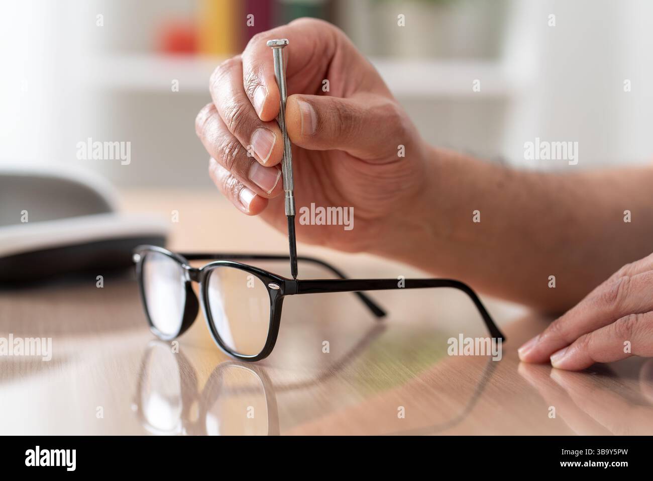 Primo piano dell'uomo che stringe gli occhiali a vite con un cacciavite su una scrivania a casa. Riparazione ottica maschio e fissaggio occhiali oculari con un cacciavite. Foto Stock